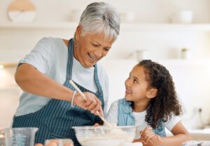 Grandmother, happy or child baking in kitchen as a happy family with young girl learning cookies recipe. Mixing cake, development or grandma smiling or teaching kid to bake with eggs, butter or flour.